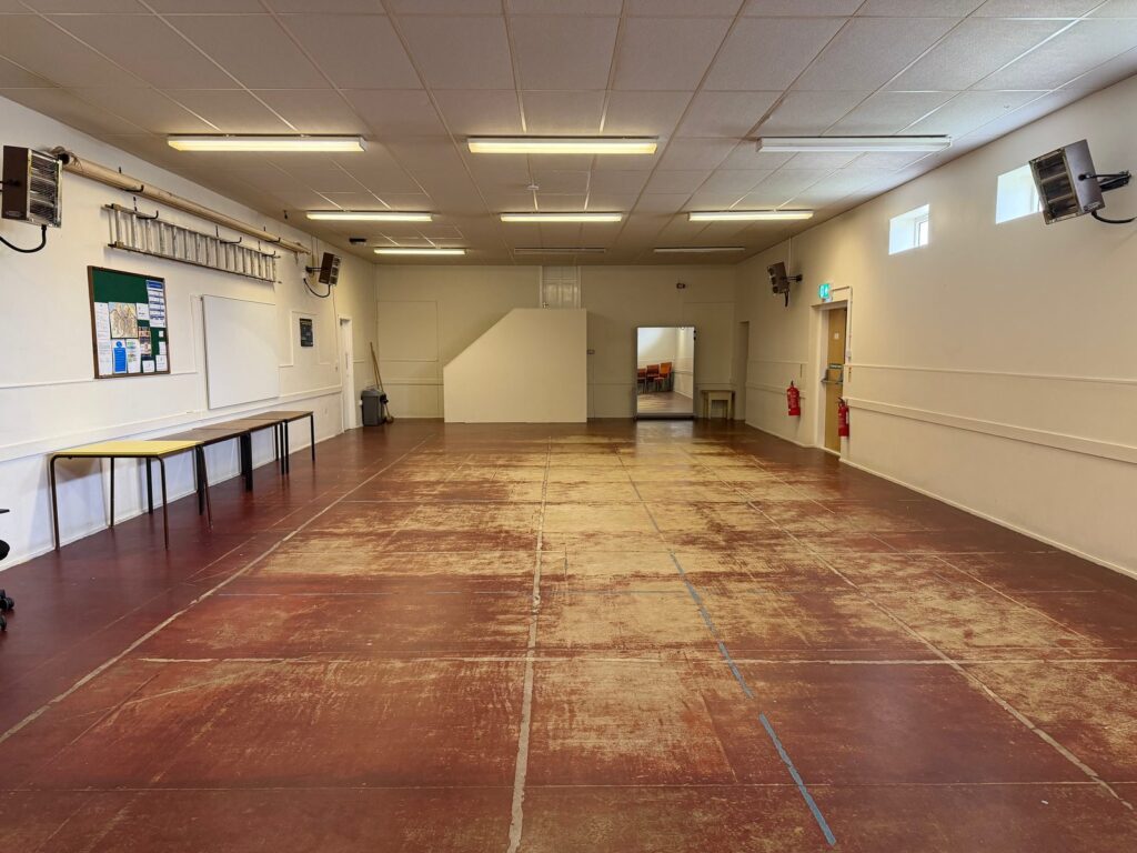 The main hall, empty, with clear floor space and the door to the training room at the far end.