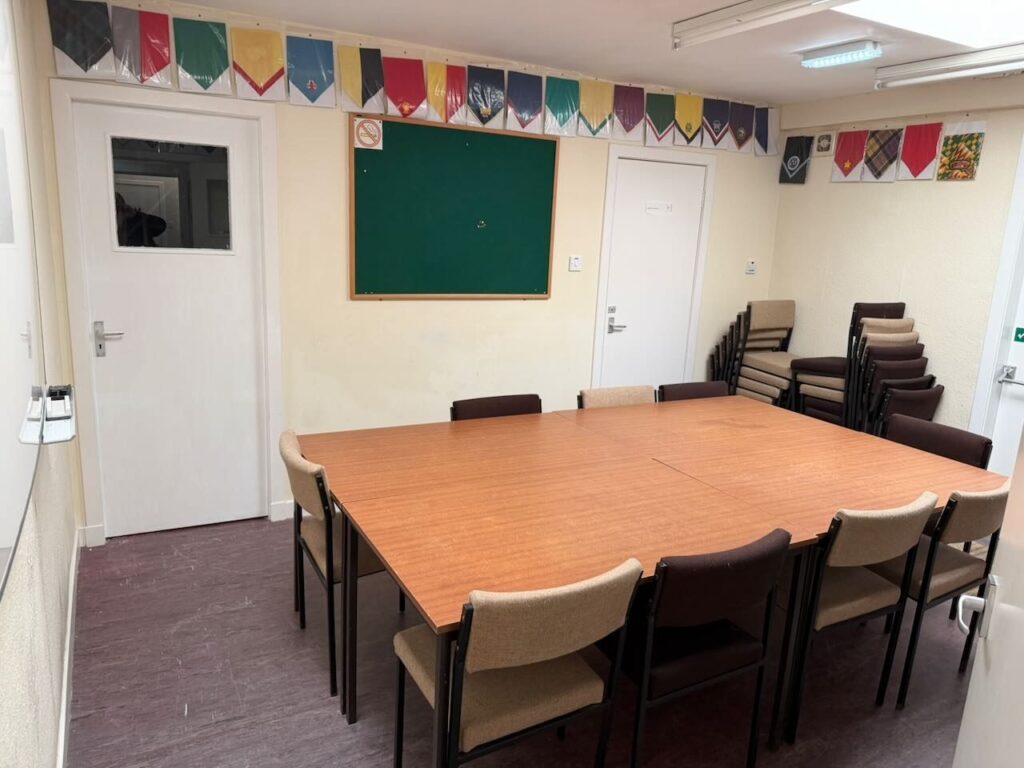 The meeting room, with a large table and chairs, a noticeboard and a row of Scout neckerchiefs along the wall.