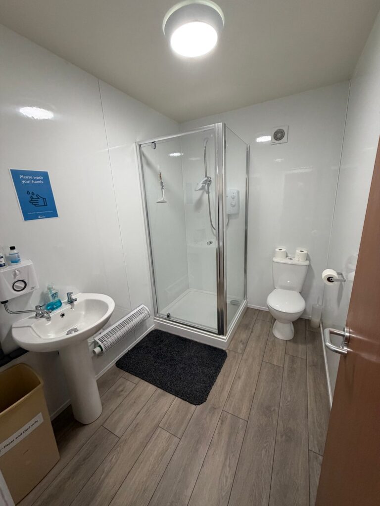 A toilet and shower room with a washbasin, a glass shower cubicle and a wood-effect floor.